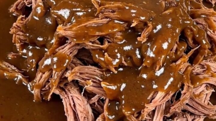A close-up of a tender, shredded beef pot roast coated in a rich, creamy peppercorn gravy on a white plate.