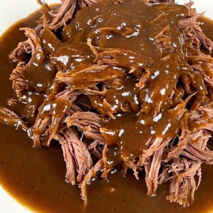 A close-up of a tender, shredded beef pot roast coated in a rich, creamy peppercorn gravy on a white plate.