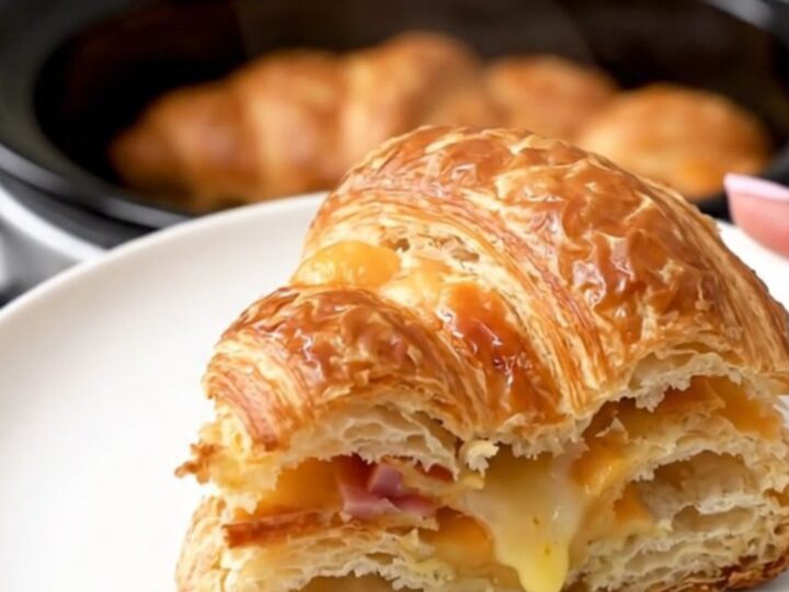A warm, golden, puffed croissant breakfast casserole slice on a white plate.
