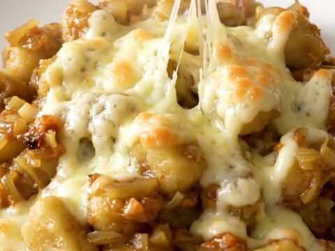 A close-up of a bowl filled with soft potato gnocchi in a rich, onion-filled broth topped with melted, bubbly Swiss cheese.
