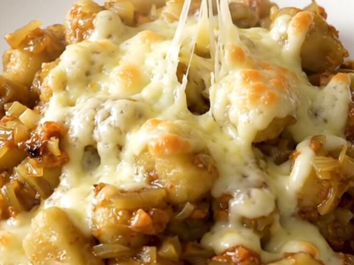 A close-up of a bowl filled with soft potato gnocchi in a rich, onion-filled broth topped with melted, bubbly Swiss cheese.