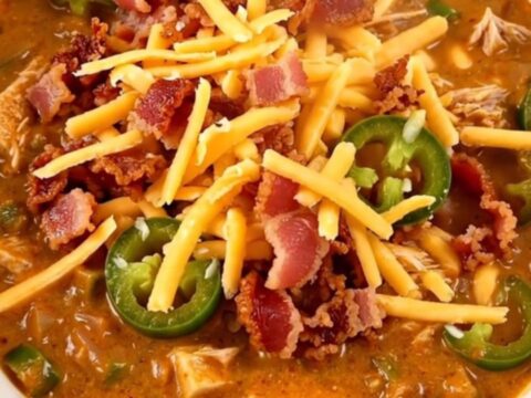 A bowl of creamy turkey chili garnished with crumbled bacon and shredded cheddar cheese.