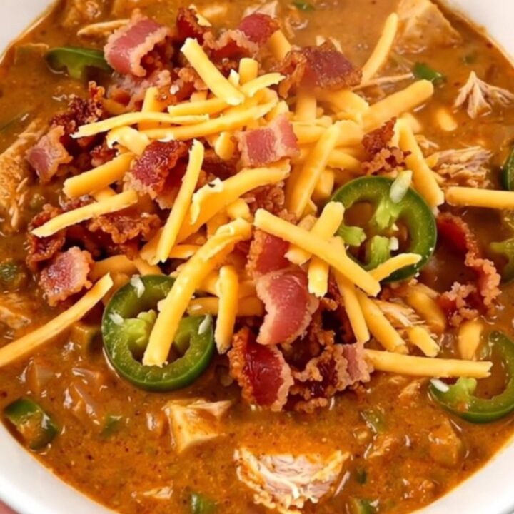 A bowl of creamy turkey chili garnished with crumbled bacon and shredded cheddar cheese.