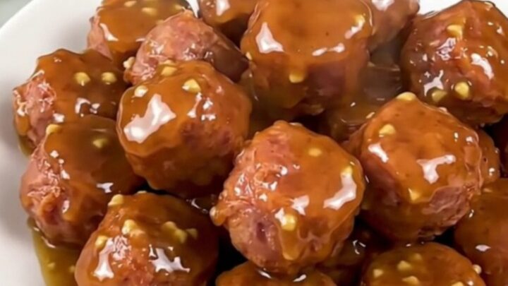 A close-up of glossy, glazed bratwurst coins in a slow cooker, looking savory and tender.