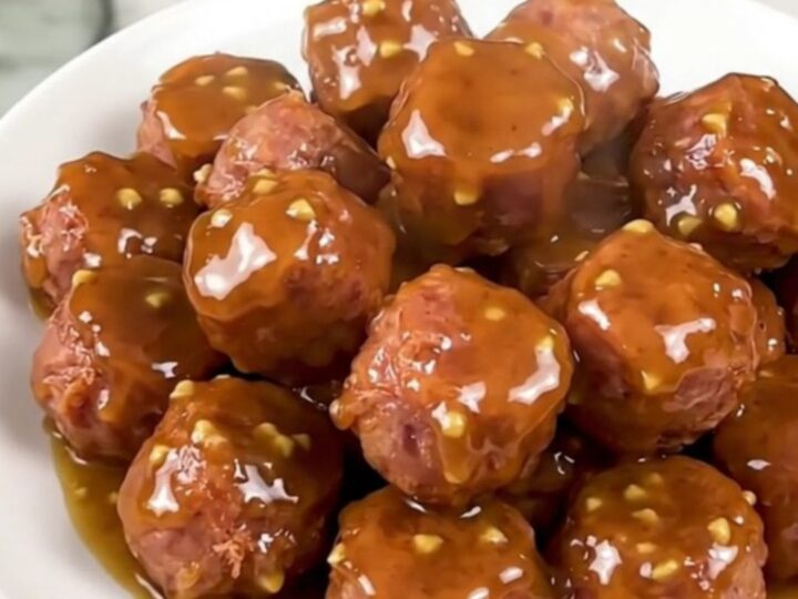 A close-up of glossy, glazed bratwurst coins in a slow cooker, looking savory and tender.