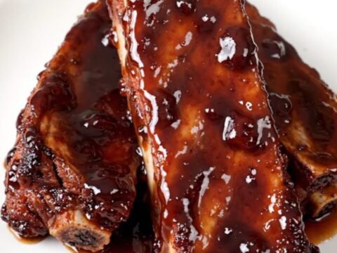 Slow cooker ribs glazed in a shiny, dark cherry cola sauce on a white plate.
