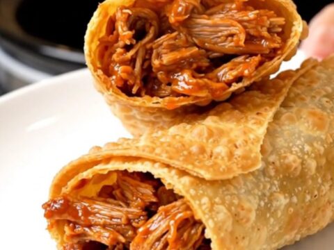 A crispy, golden-brown chimichanga sliced in half on a white plate, showing a steaming, shredded pork filling.