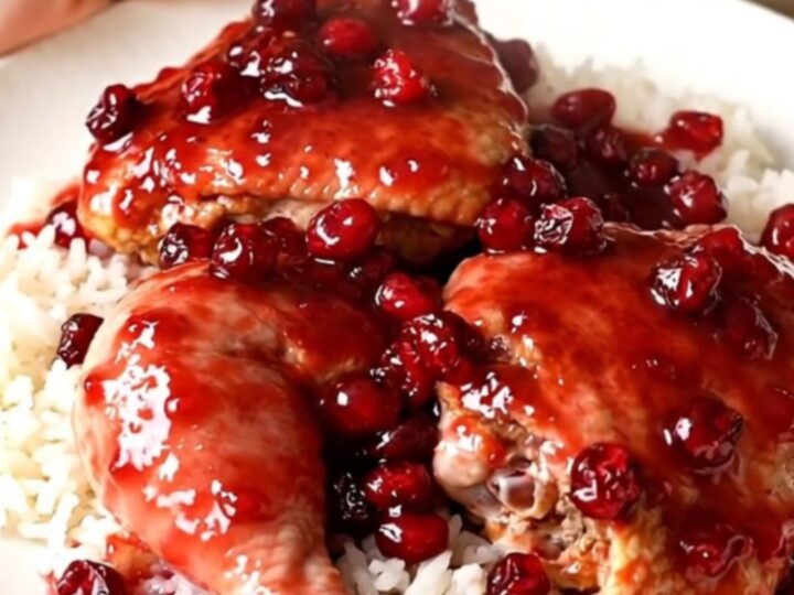 A top-down view of raw chicken thighs, diced onions, and cranberry sauce arranged in a slow cooker.