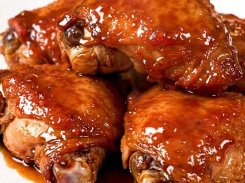 A close-up of glossy, tender Korean BBQ chicken thighs served on a white plate with a dark, savory glaze.