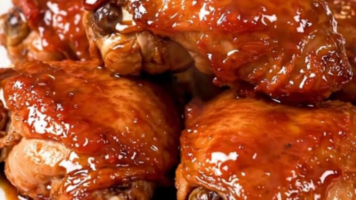 A close-up of glossy, tender Korean BBQ chicken thighs served on a white plate with a dark, savory glaze.