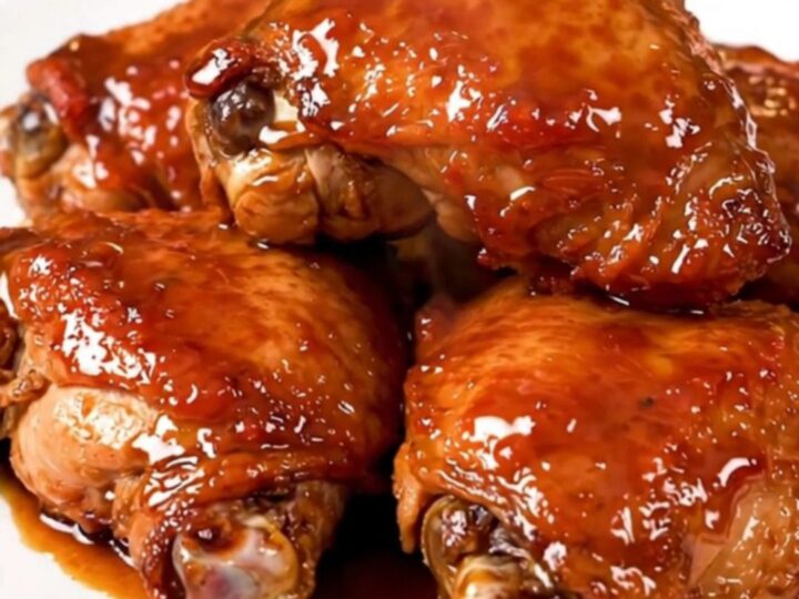 A close-up of glossy, tender Korean BBQ chicken thighs served on a white plate with a dark, savory glaze.