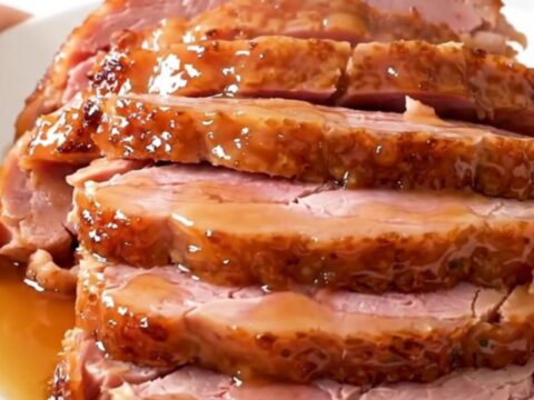 A glossy, glazed spiral-cut ham served on a white plate with visible steam rising from the meat.