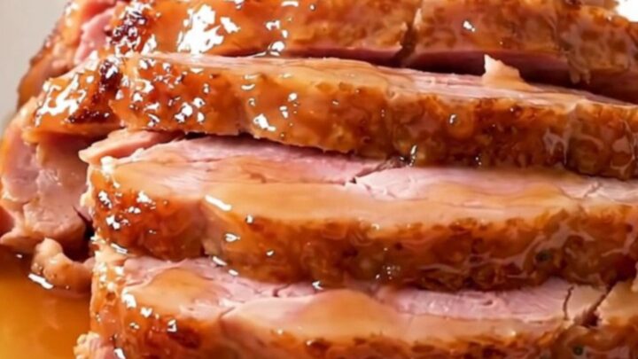 A glossy, glazed spiral-cut ham served on a white plate with visible steam rising from the meat.