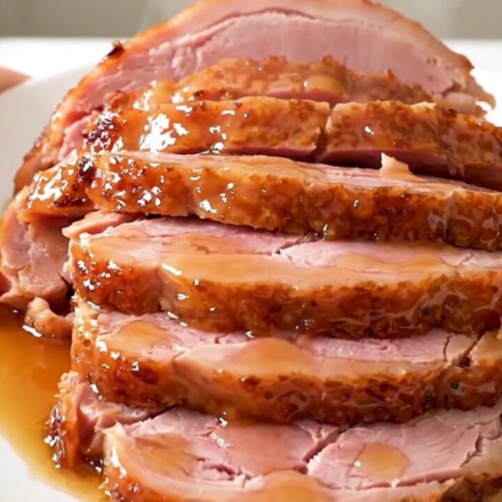 A glossy, glazed spiral-cut ham served on a white plate with visible steam rising from the meat.