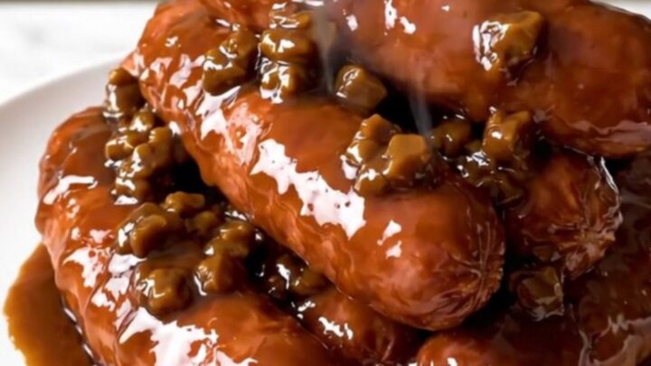 A close-up of glossy, glazed kielbasa pieces served on a white plate in a warm, inviting kitchen.