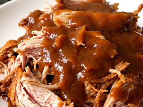 A top-down view of a slow cooker filled with raw chicken thighs, red onions, and chipotle peach barbecue sauce.
