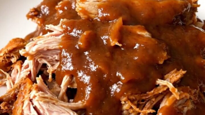 A top-down view of a slow cooker filled with raw chicken thighs, red onions, and chipotle peach barbecue sauce.