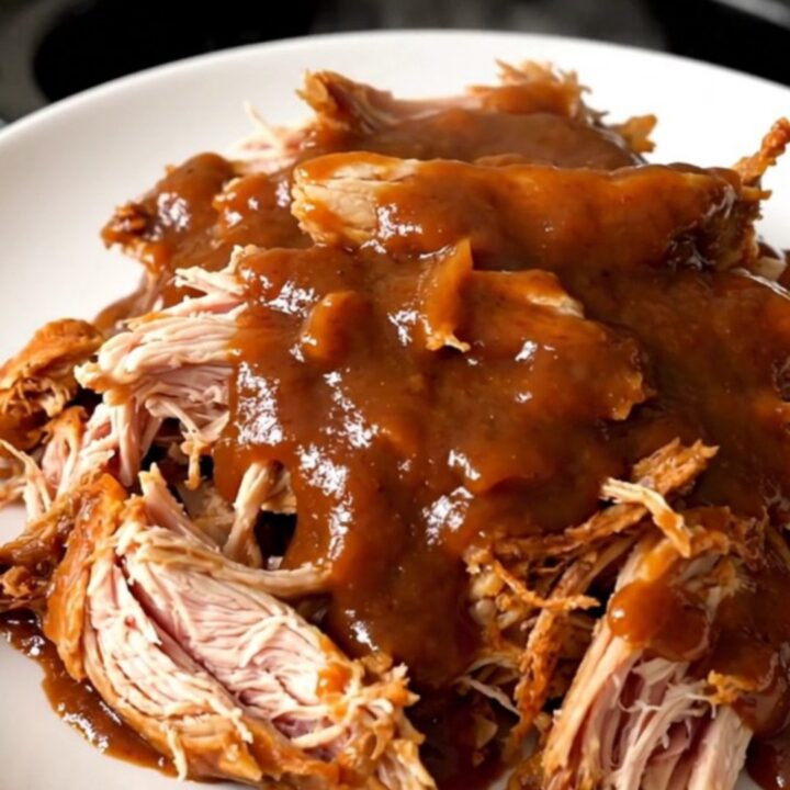 A top-down view of a slow cooker filled with raw chicken thighs, red onions, and chipotle peach barbecue sauce.