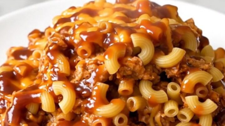A close-up of a slow cooker filled with creamy pulled pork macaroni bake on a white speckled quartz countertop.