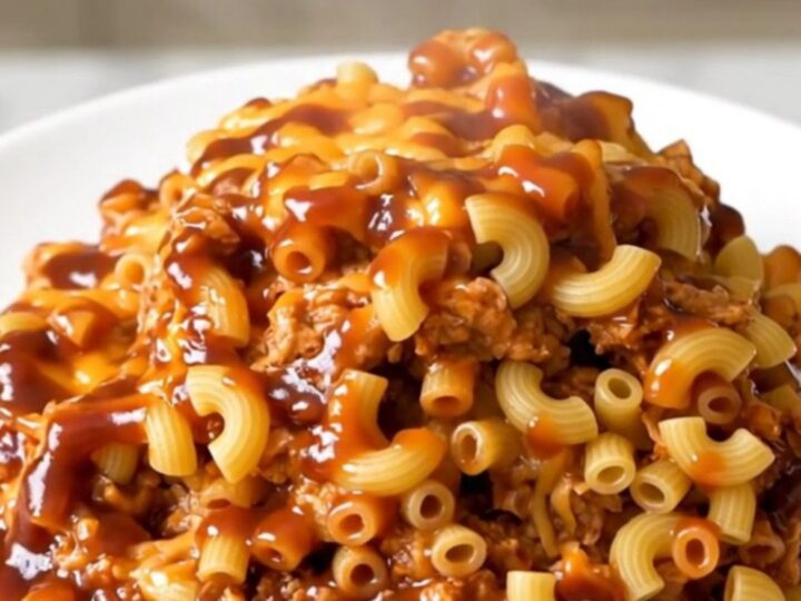A close-up of a slow cooker filled with creamy pulled pork macaroni bake on a white speckled quartz countertop.