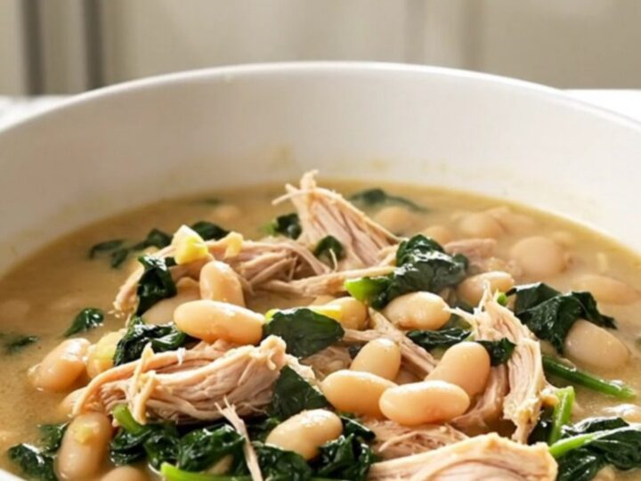 A white bowl filled with steaming Tuscan chicken and white bean stew with visible pieces of shredded chicken and spinach.