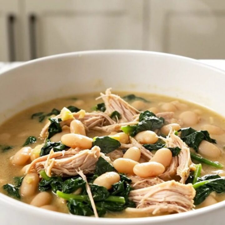 A white bowl filled with steaming Tuscan chicken and white bean stew with visible pieces of shredded chicken and spinach.