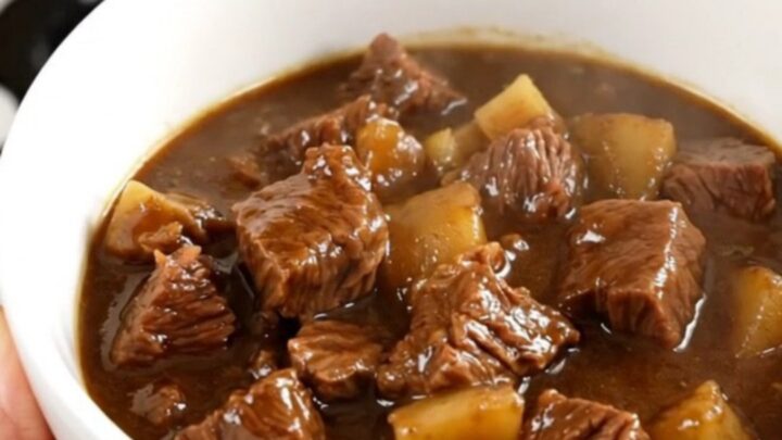 A bowl of rich stout beef stew with tender chunks of beef, carrots, and potatoes in a dark, glossy sauce.