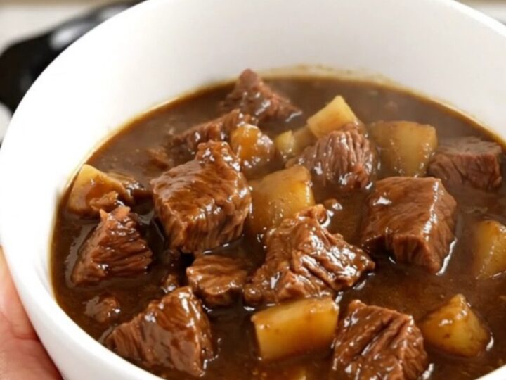 A bowl of rich stout beef stew with tender chunks of beef, carrots, and potatoes in a dark, glossy sauce.