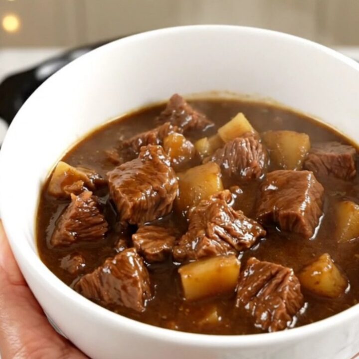 A bowl of rich stout beef stew with tender chunks of beef, carrots, and potatoes in a dark, glossy sauce.