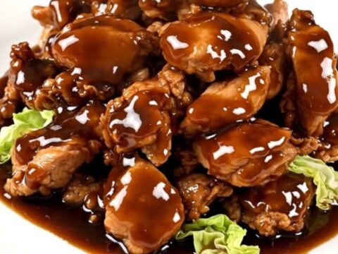 A top-down view of raw chicken, shredded cabbage, and hoisin sauce being layered into a black slow cooker.