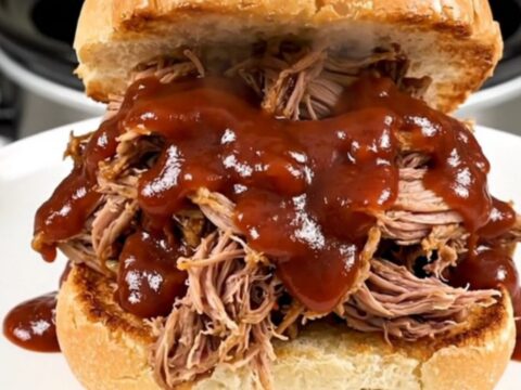 A close-up of a tender, saucy pulled pork sandwich on a toasted brioche bun, showcasing the glossy texture.