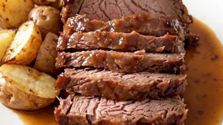Slow cooker rosemary Dijon pot roast served on a white plate with glazed baby red potatoes.