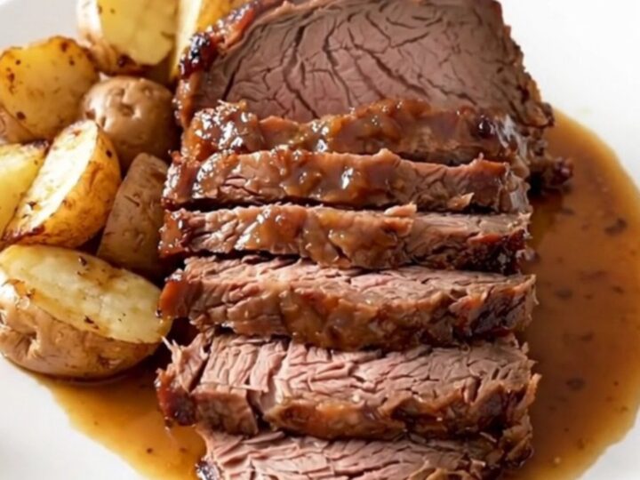Slow cooker rosemary Dijon pot roast served on a white plate with glazed baby red potatoes.