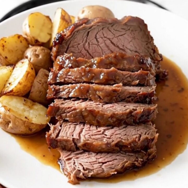 Slow cooker rosemary Dijon pot roast served on a white plate with glazed baby red potatoes.