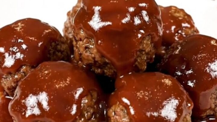 A top-down view of a black slow cooker filled with glazed turkey meatballs on a speckled quartz countertop.