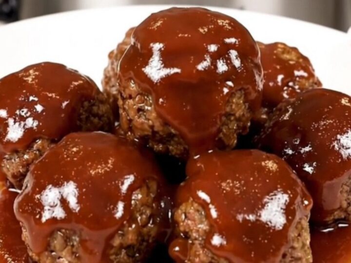 A top-down view of a black slow cooker filled with glazed turkey meatballs on a speckled quartz countertop.