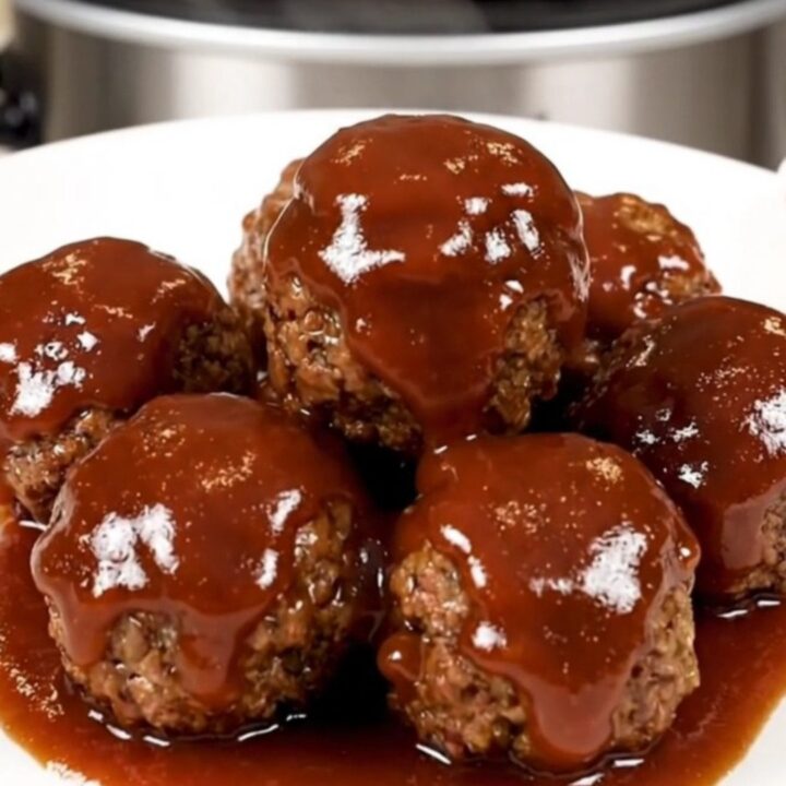 A top-down view of a black slow cooker filled with glazed turkey meatballs on a speckled quartz countertop.