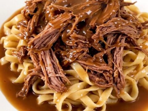 A delicious slow cooker ranch and onion chuck roast served over egg noodles on a white plate.