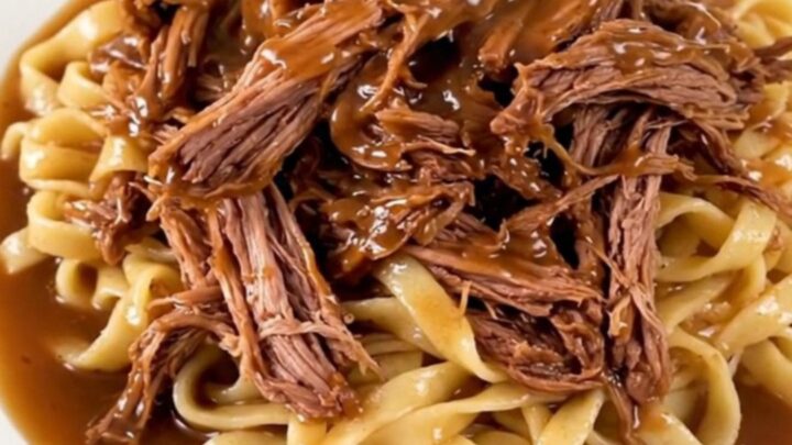 A delicious slow cooker ranch and onion chuck roast served over egg noodles on a white plate.