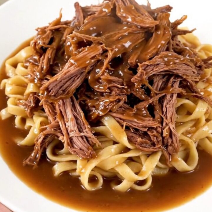 A delicious slow cooker ranch and onion chuck roast served over egg noodles on a white plate.