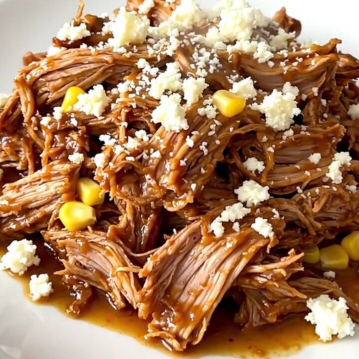A plate of shredded pulled pork mixed with corn and topped with crumbled cotija cheese.