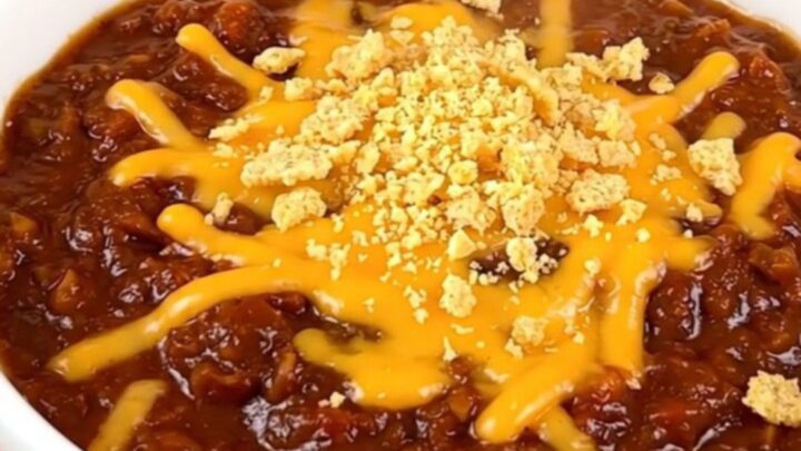 A close-up of a bowl of slow cooker barbecue ranch beef chili topped with melted cheddar cheese and crushed corn chips.