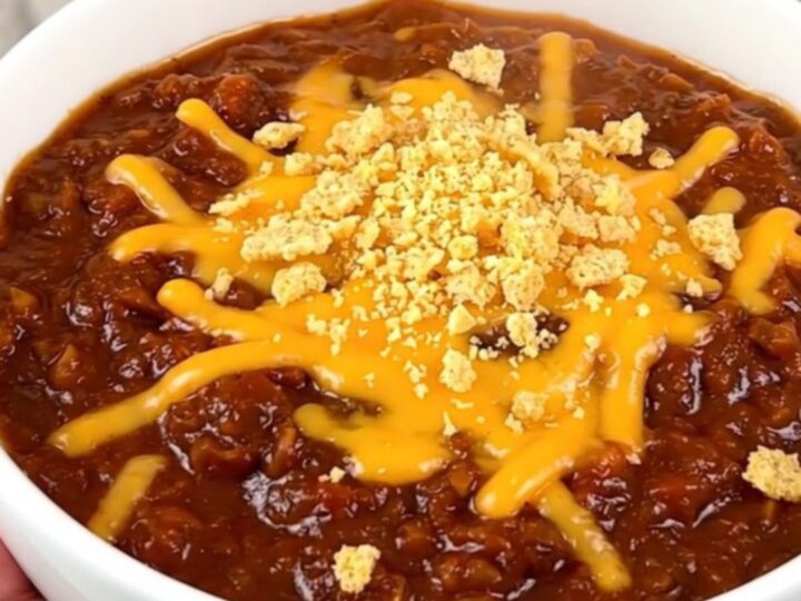A close-up of a bowl of slow cooker barbecue ranch beef chili topped with melted cheddar cheese and crushed corn chips.