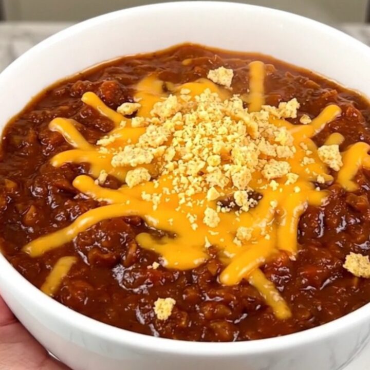 A close-up of a bowl of slow cooker barbecue ranch beef chili topped with melted cheddar cheese and crushed corn chips.