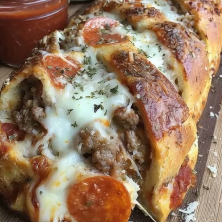 A golden-brown braided pizza bread loaf fresh out of the oven, garnished with melted parmesan and fresh herbs on a wooden