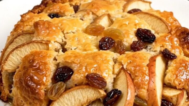 A close-up of warm, golden apple cobbler in a white bowl with visible raisins and cinnamon.