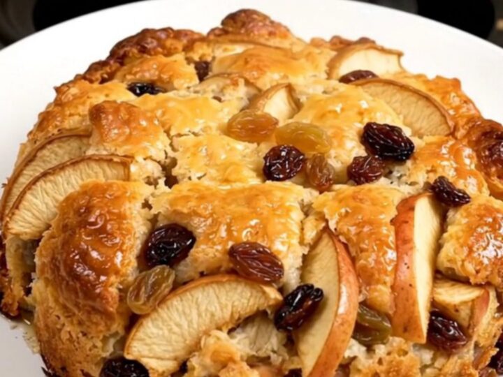 A close-up of warm, golden apple cobbler in a white bowl with visible raisins and cinnamon.