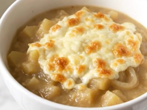 A steaming bowl of creamy French onion potato chowder topped with melted cheese on a white background.