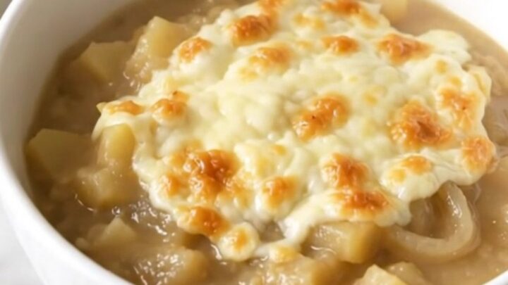 A steaming bowl of creamy French onion potato chowder topped with melted cheese on a white background.