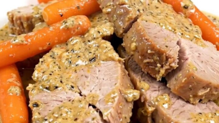 A close-up of sliced creamy ranch pork tenderloin and cooked baby carrots on a white plate.